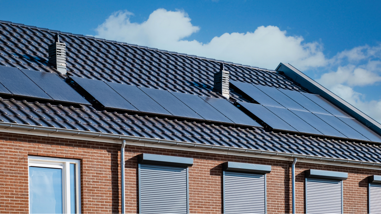 Zonnepanelen op een rood tegel dak van een woning met een blauwe lucht op de achtergrond.