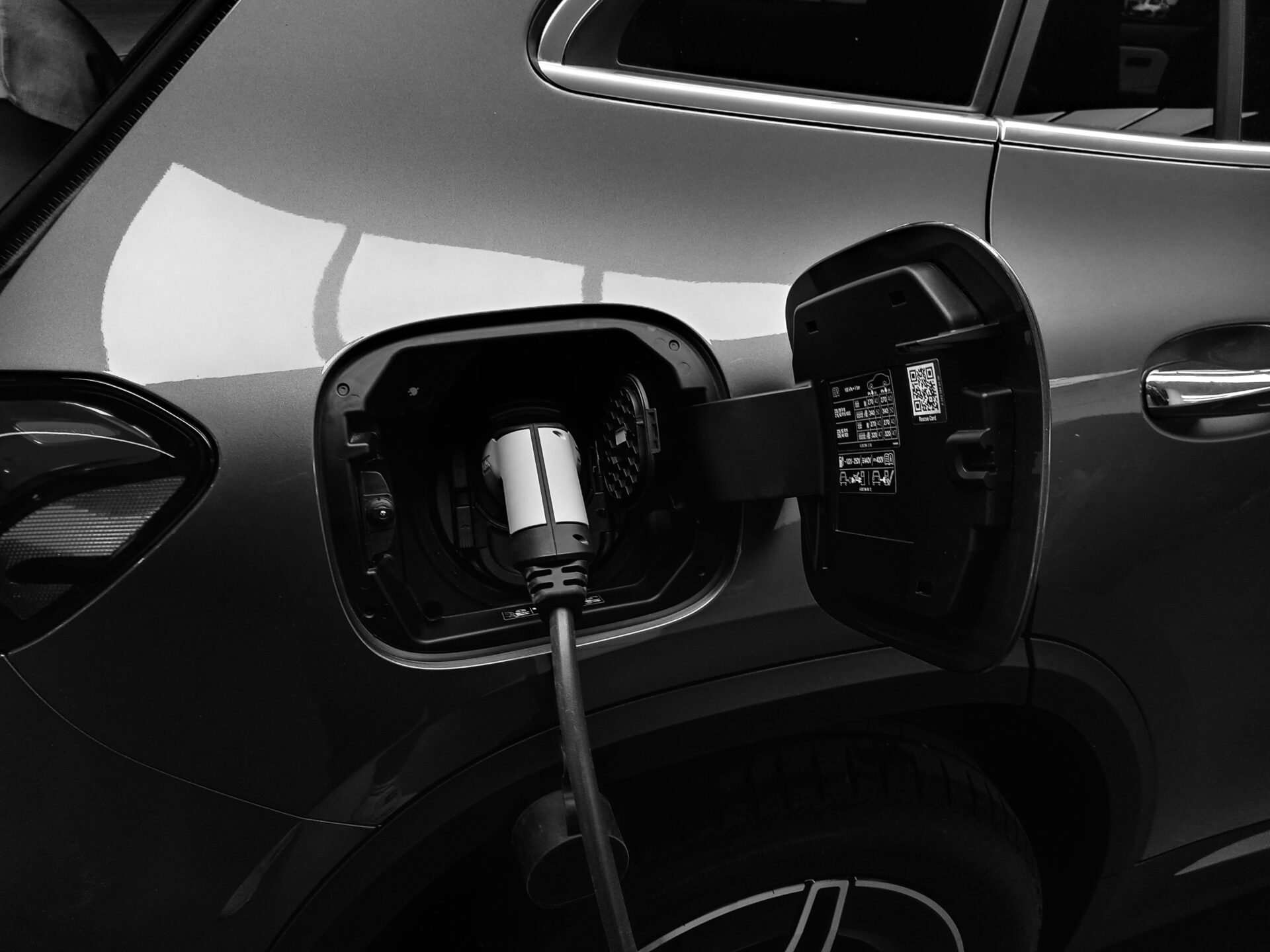 Zwart-wit close-up van een elektrische auto met een laadkabel aangesloten op de laadpoort.