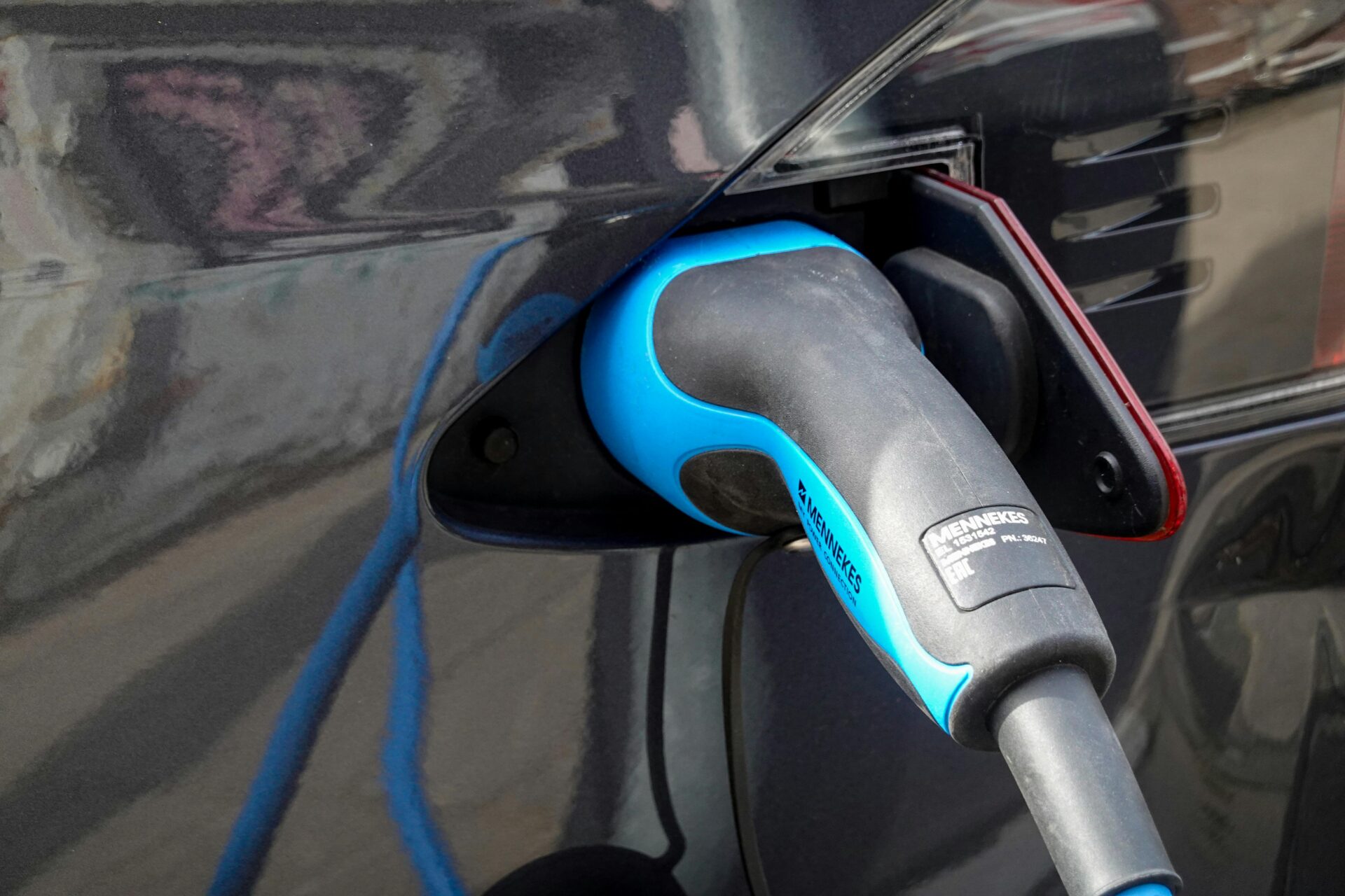 Close-up van een blauwe laadkabel aangesloten op een donkere elektrische auto.