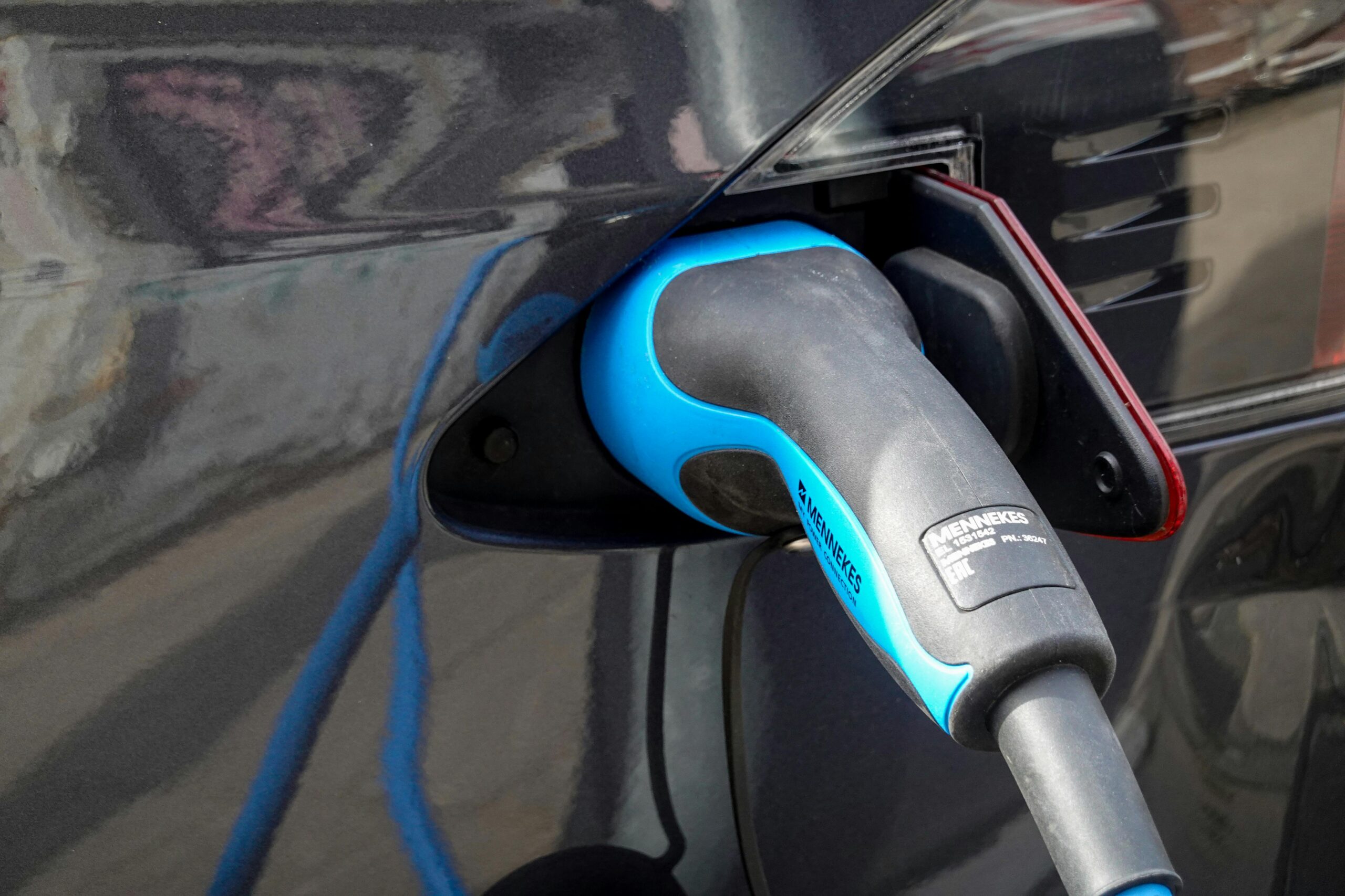 Close-up van een blauwe laadkabel aangesloten op een donkere elektrische auto.